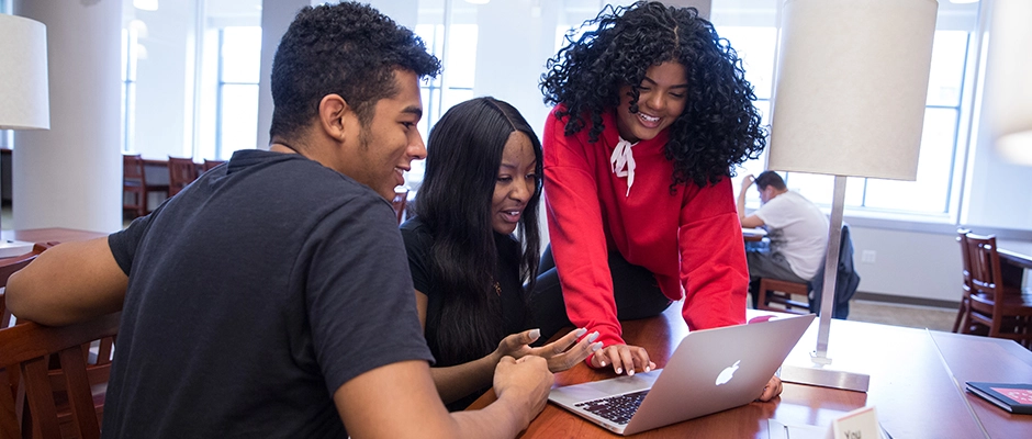 Students in the Library smiling and looking at a computer